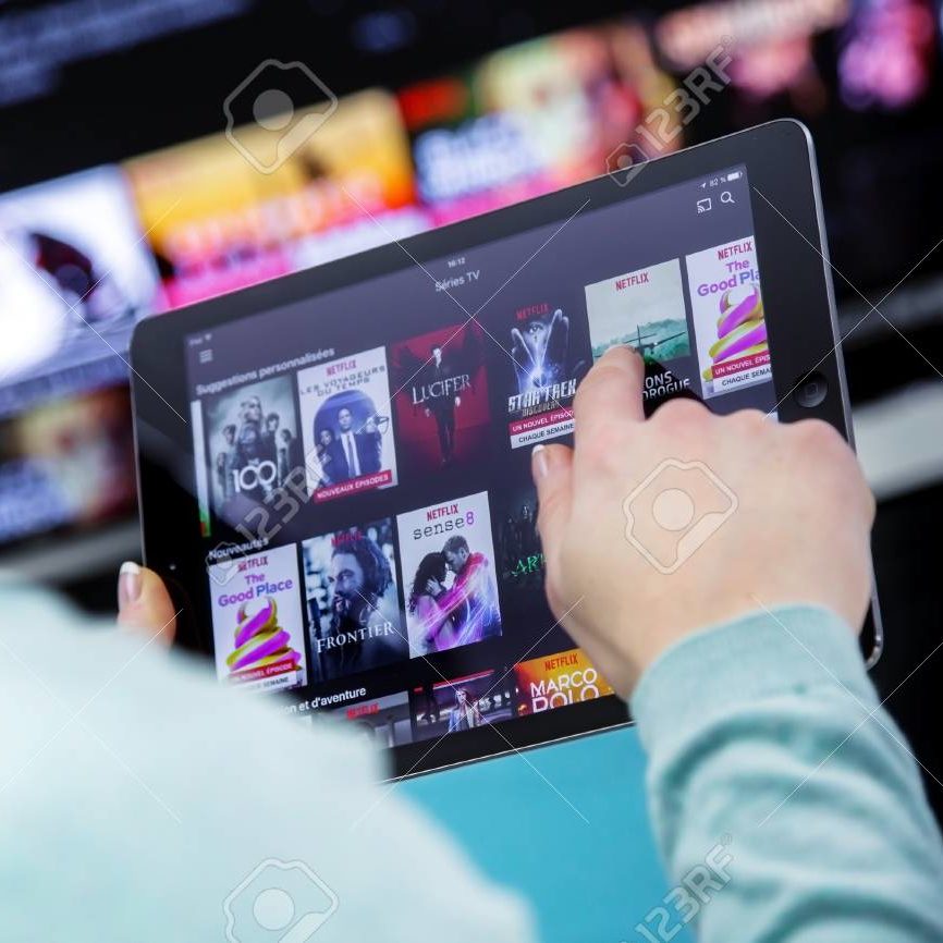 Benon, France - January 21, 2018: Woman Holding a touch pad and switching channels on France Netflix HomePage. with TV set on background. Netflix Inc. is an American multinational entertainment company founded on 1997